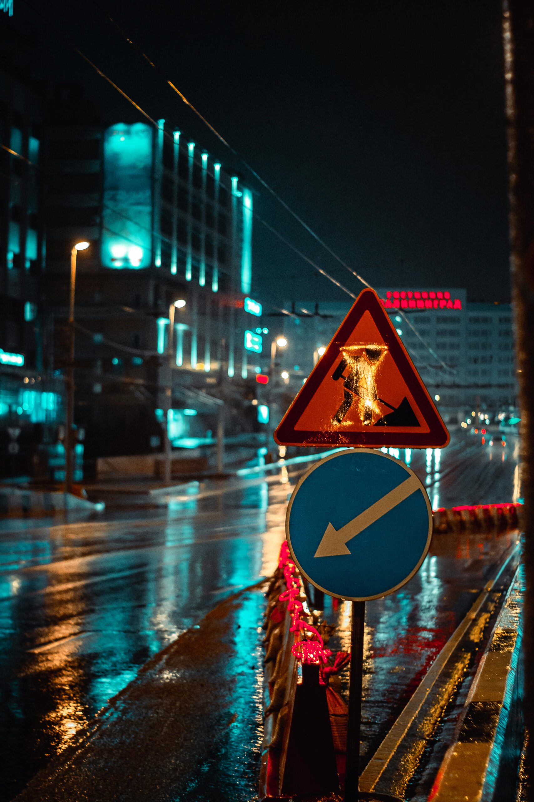 Illuminated city street at night with wet reflections and vibrant traffic signs.